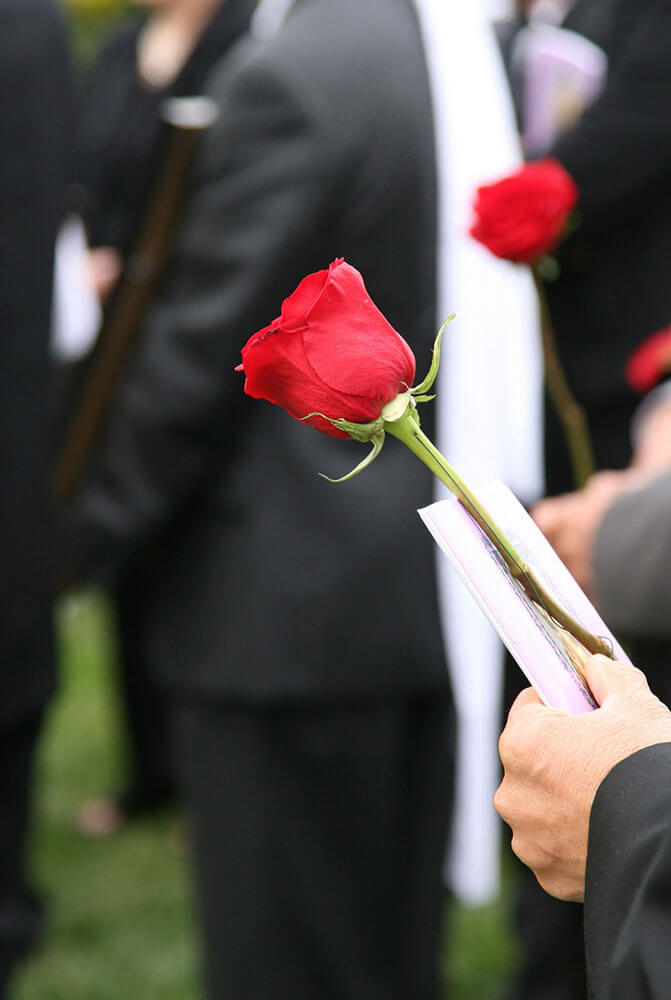 Eine Gruppe von Menschen hält rote Rosen bei einer Beerdigung